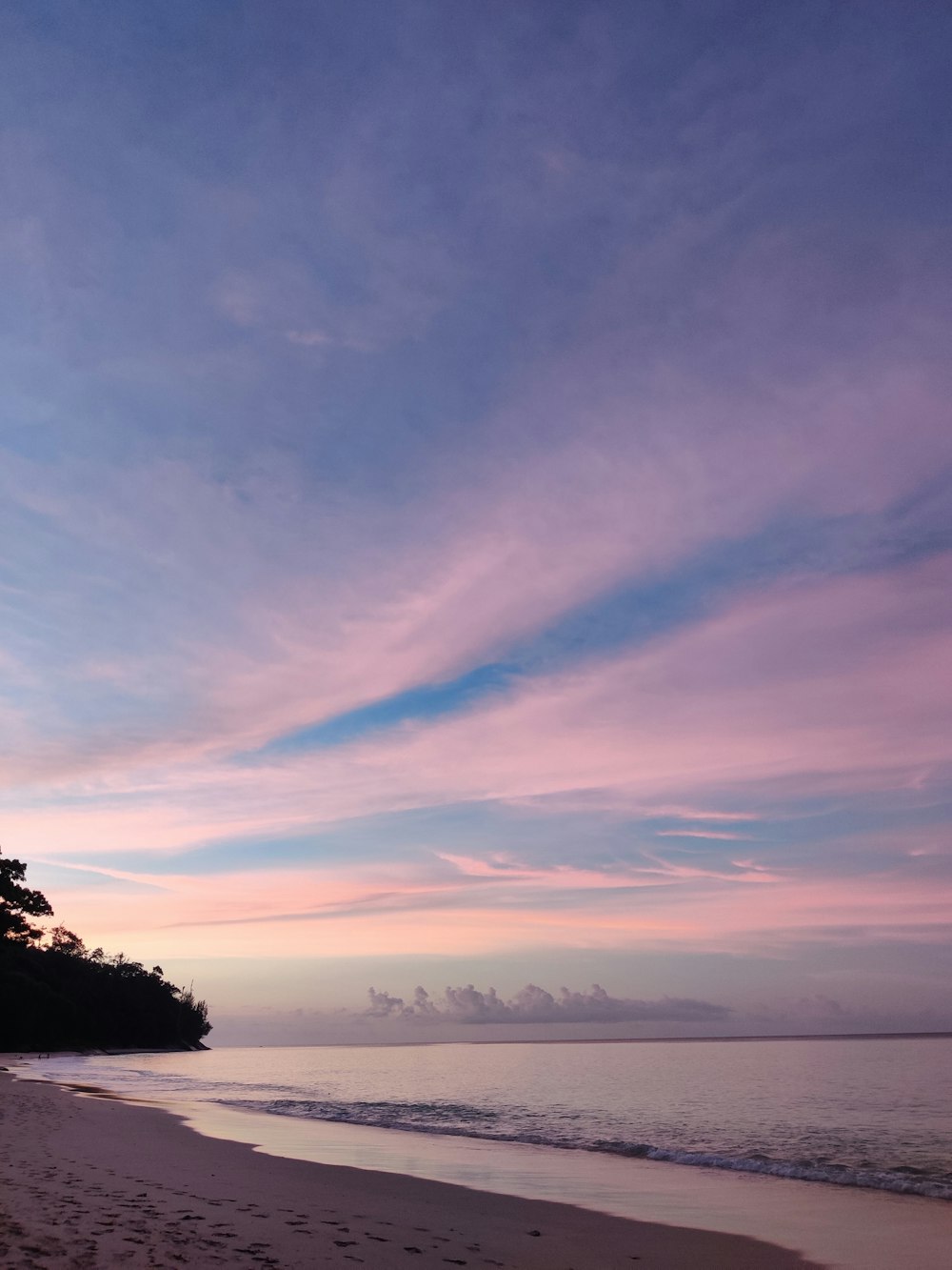 a beach at sunset with footprints in the sand