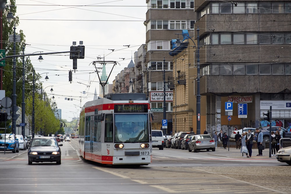 Ein rot-weißer Bus fährt eine Straße neben hohen Gebäuden entlang