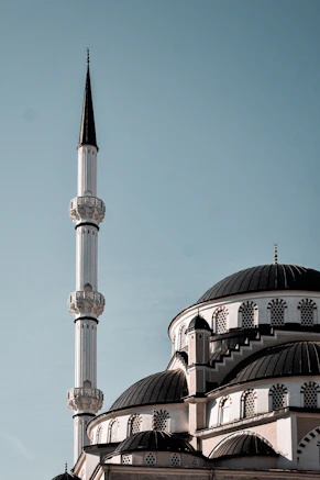 A white mosque with dark domes and a tall minaret against a clear sky