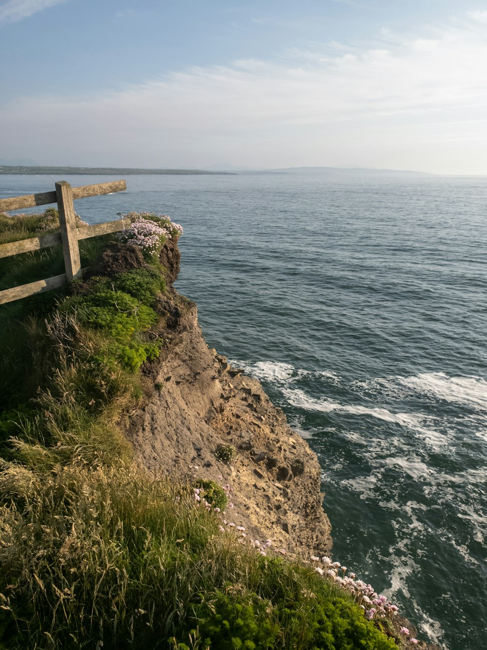a wooden bench sitting on top of a cliff next to the ocean