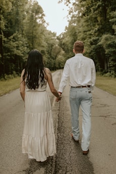 a man and woman walking down a road holding hands