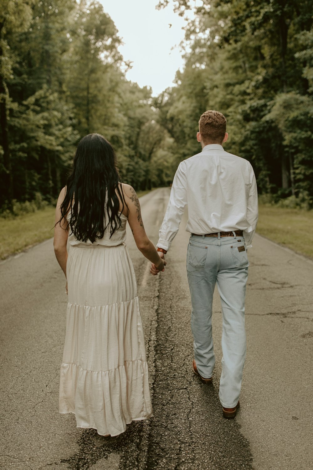 a man and woman walking down a road holding hands