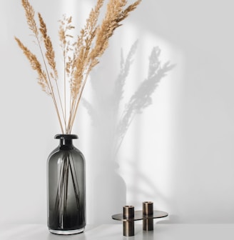 a black vase with some dry grass in it