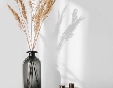 a black vase with some dry grass in it