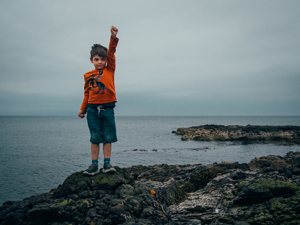 a young boy standing on a rock by the ocean