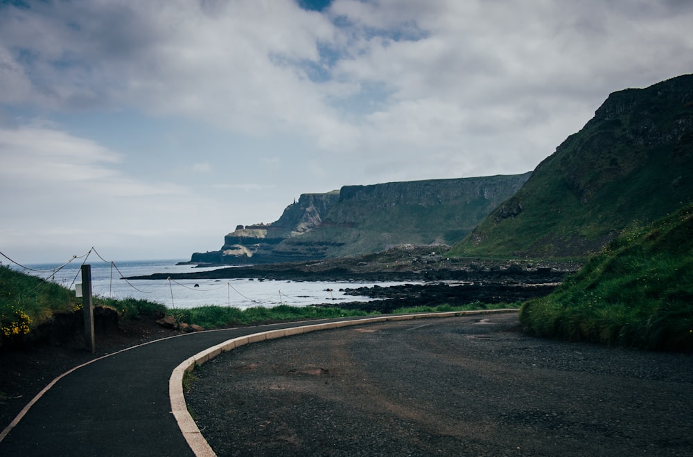 a curved road next to the ocean on a cloudy day