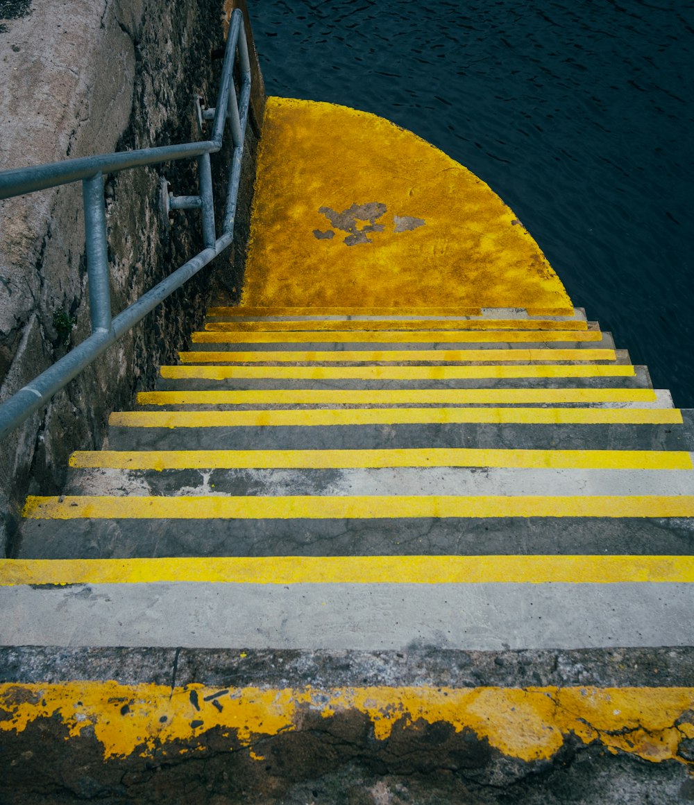 a set of stairs with yellow painted steps next to a body of water