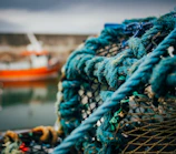 Close-up of a traditional fishing net drying on a rustic boat, with gentle waves in the background.
