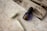 A facial roller made of jade and a small bottle of a skincare product are placed on a marbled surface. The blue bottle has a dropper and is labeled with gold text. Beside these items, there is an open book with monochrome photography and a delicate gold chain positioned across it.