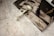 A facial roller, an essential oil bottle, and a gold necklace are placed on an open magazine with a monochrome print on a marble surface.
