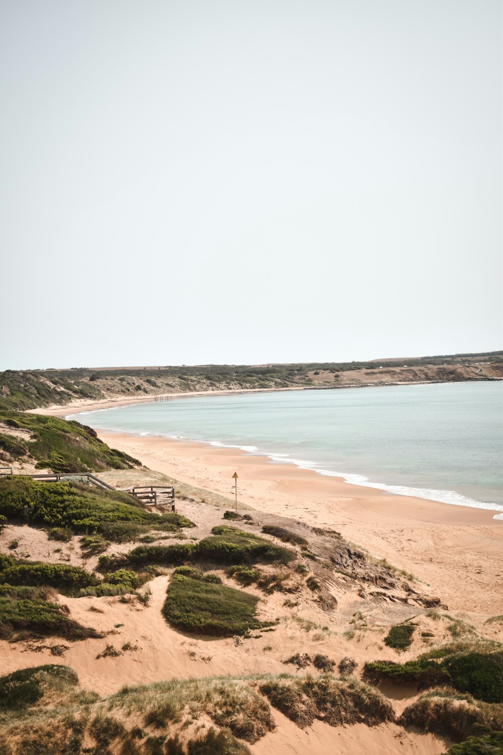 a sandy beach with a bench next to the ocean