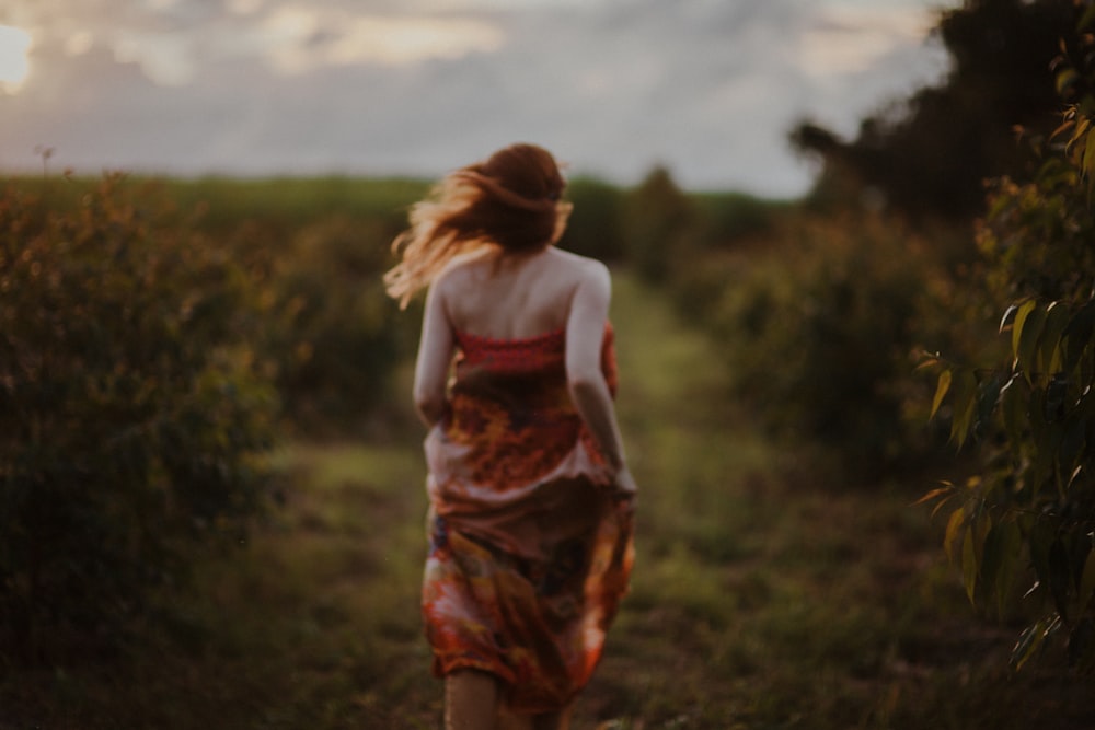a woman walking down a dirt road in a dress