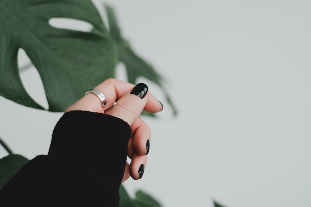 a woman's hand holding a ring in front of a plant