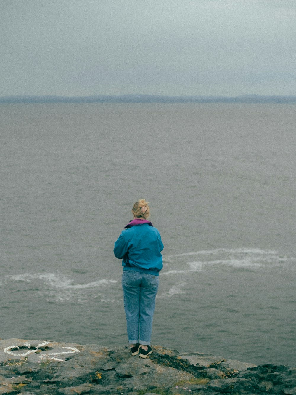 a woman standing on top of a rock next to the ocean