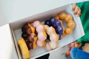 Overhead shot of hands reaching into a box filled with various uniquely topped Smithfield Ave Donuts.