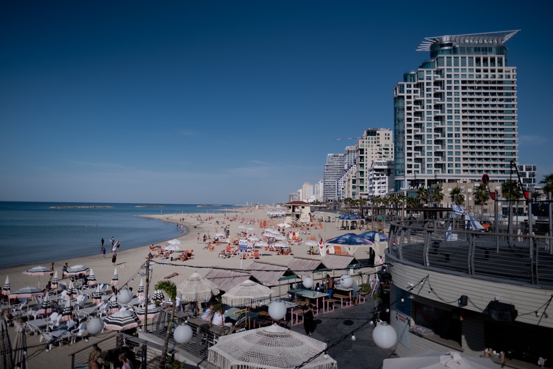 a crowded beach with umbrellas and buildings in the background, Tel Aviv.
