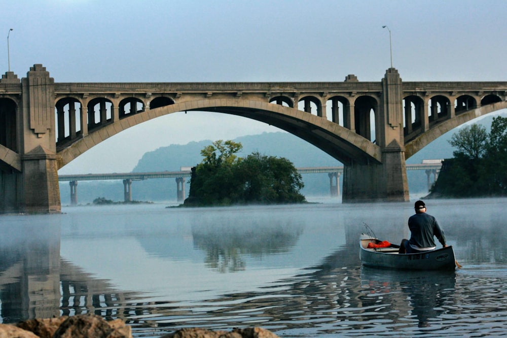 a man sitting in a boat on a river under a bridge