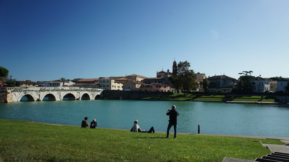 a group of people sitting on the grass near a body of water