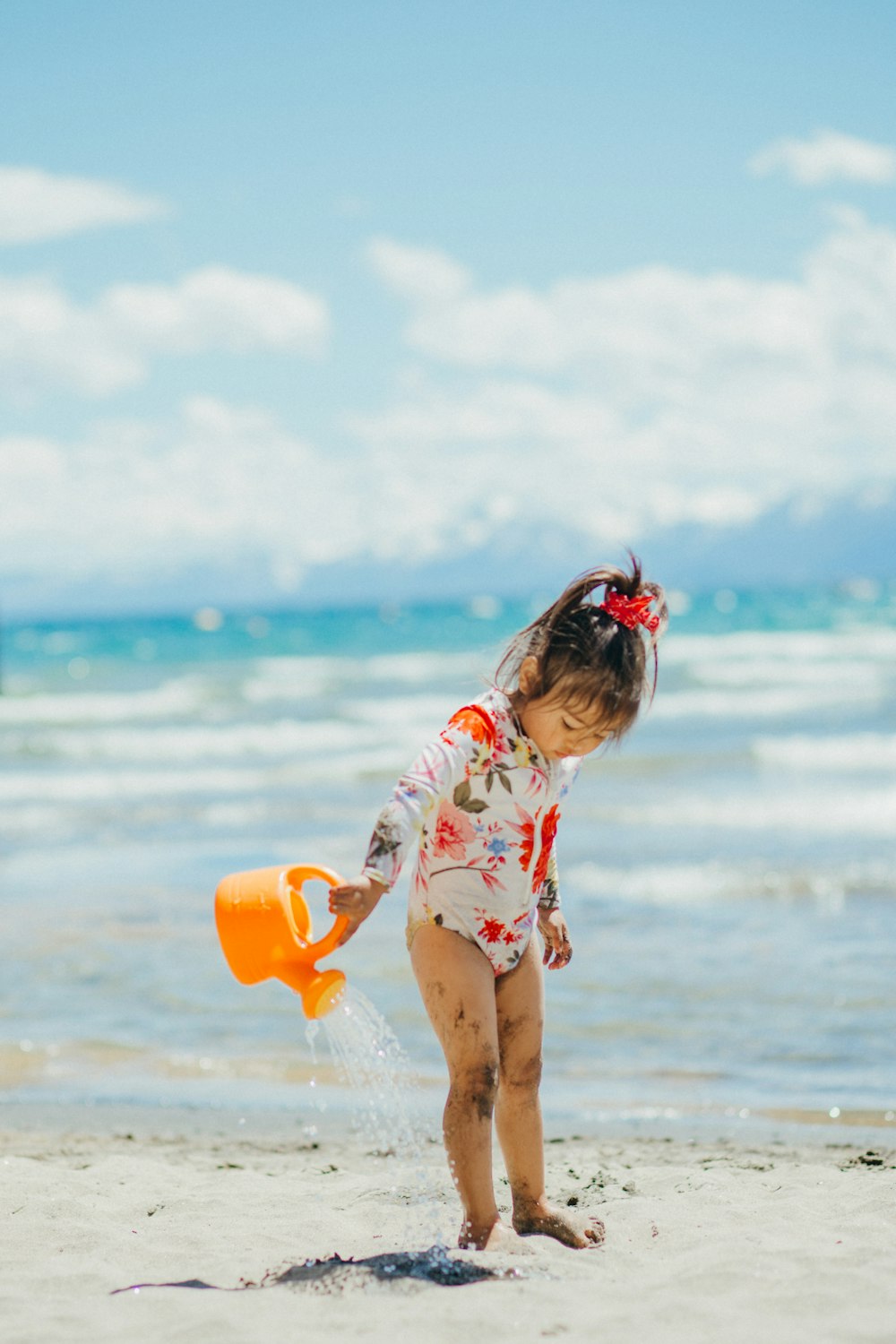 girl in white and pink floral shirt holding orange plastic bucket on beach during daytime