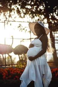 a pregnant woman wearing a white dress and a straw hat