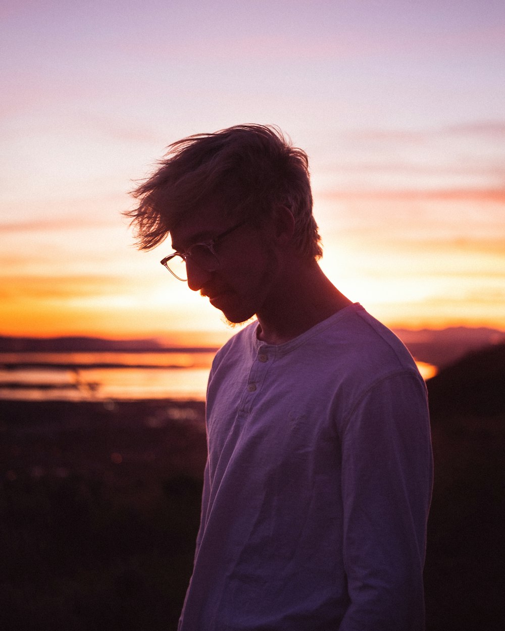 a man with glasses standing in front of a sunset