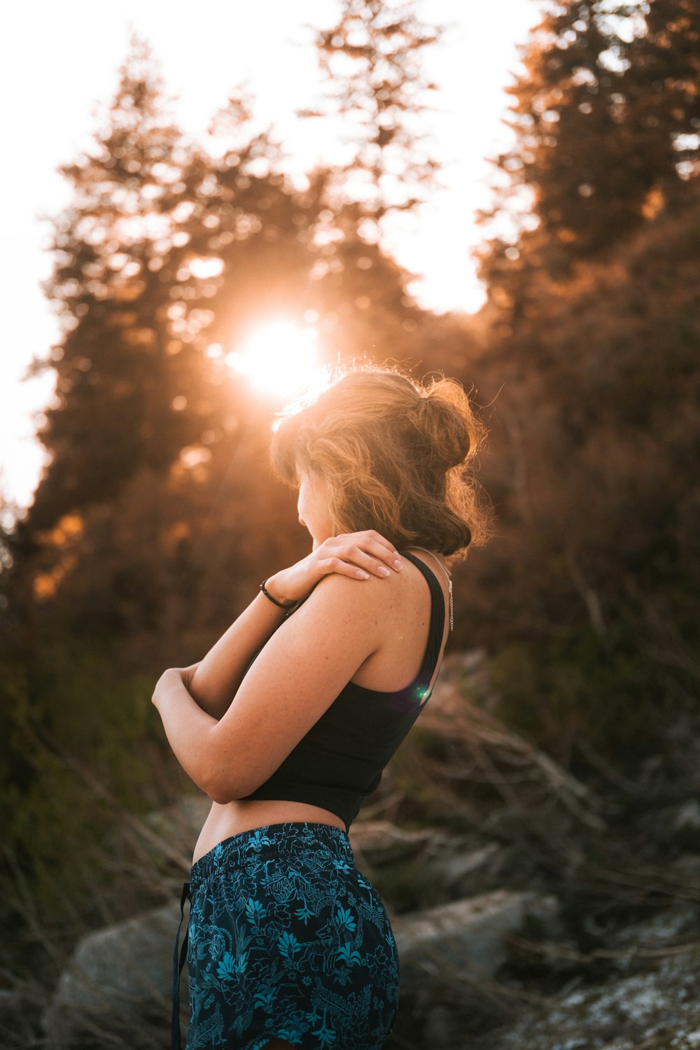 a woman standing in front of a forest at sunset