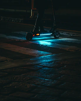 A sleek electric scooter gliding through a vibrant city street at dusk, with glowing blue lights highlighting its modern design.