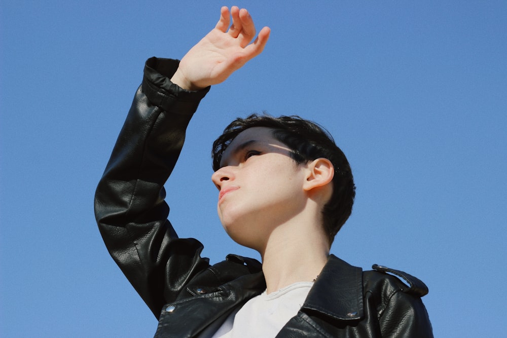 a woman in a black leather jacket is holding her hand up