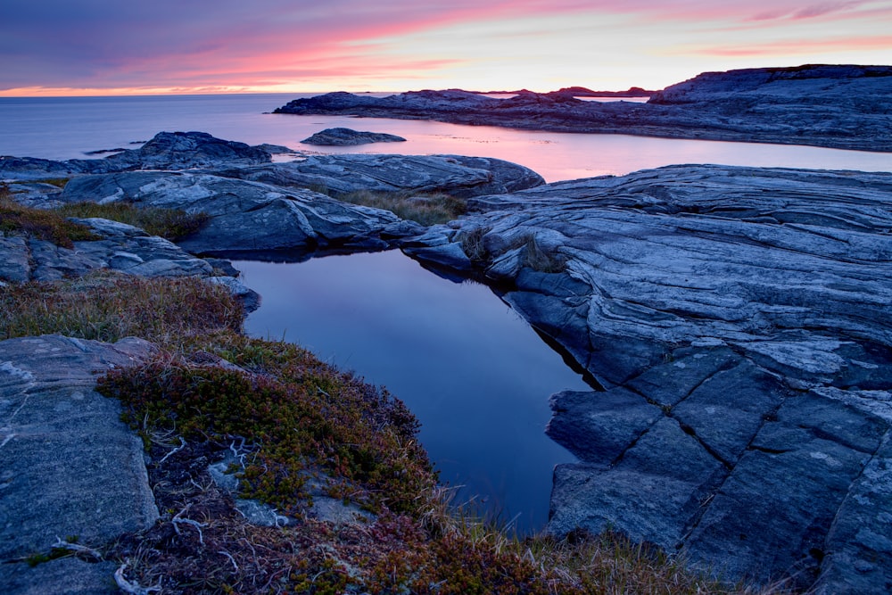 a rocky shore with a body of water at sunset