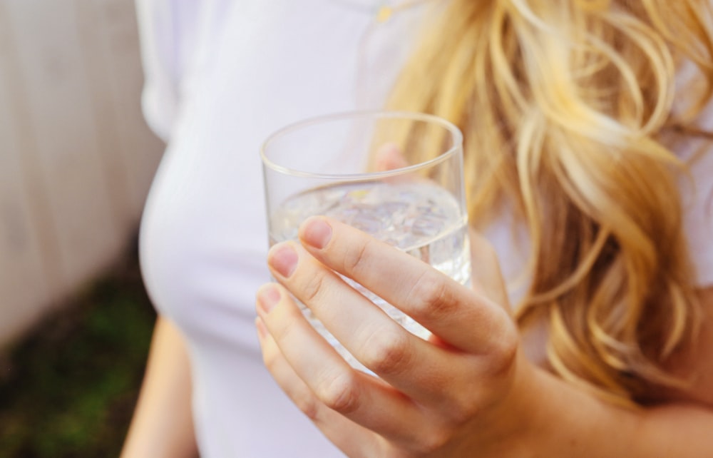 Una mujer sosteniendo un vaso de agua en la mano