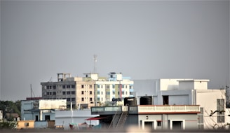 Various residential buildings of different heights and colors are seen under a clear sky. The buildings include apartments and smaller structures with visible water tanks on some roofs.