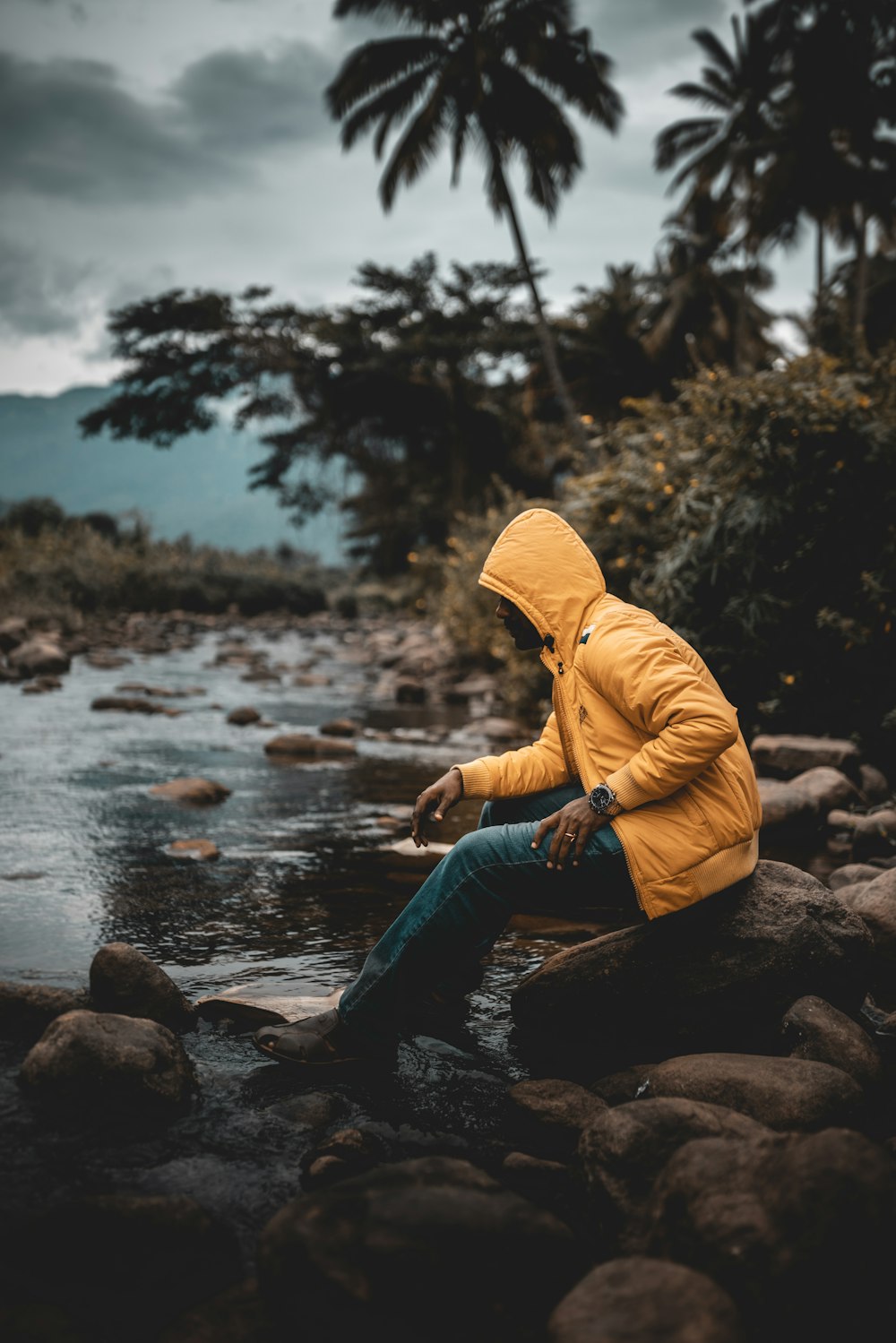 a man in a yellow jacket is sitting on a rock