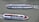 Two modern passenger boats are cruising on a body of water. Both boats have sleek designs with open viewing decks and have a white and blue color scheme. The vessels are moving parallel to each other, and there are visible ripples in the water created by their motion.