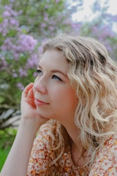 a woman sitting in front of a tree with her hand on her chin