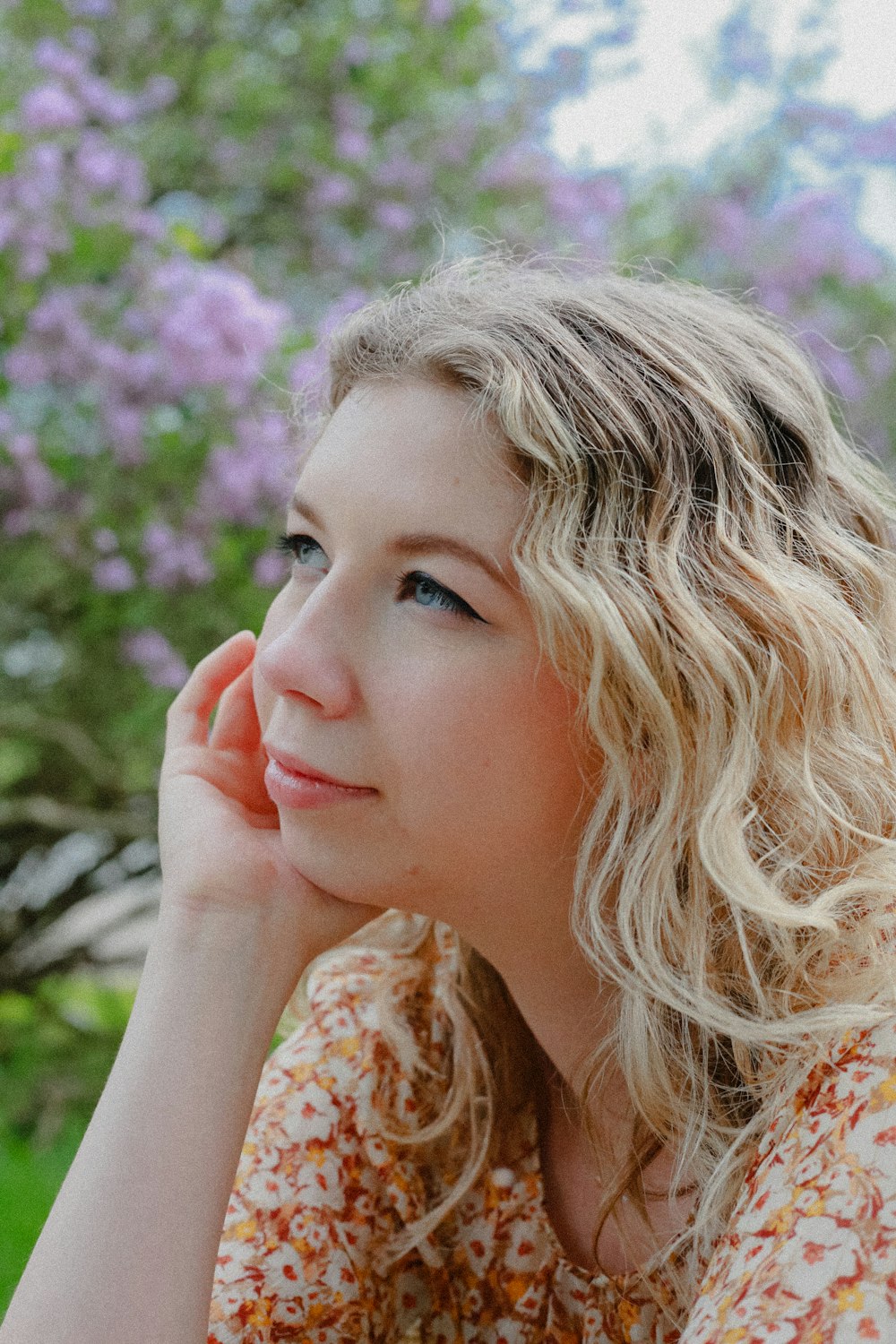 a woman sitting in front of a tree with her hand on her chin