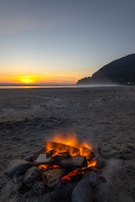 A serene beach at sunset with travelers relaxing and sharing stories around a bonfire.