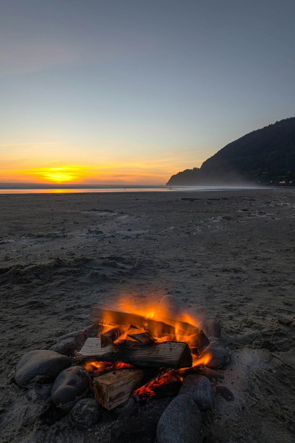 a campfire on a beach with a sunset in the background