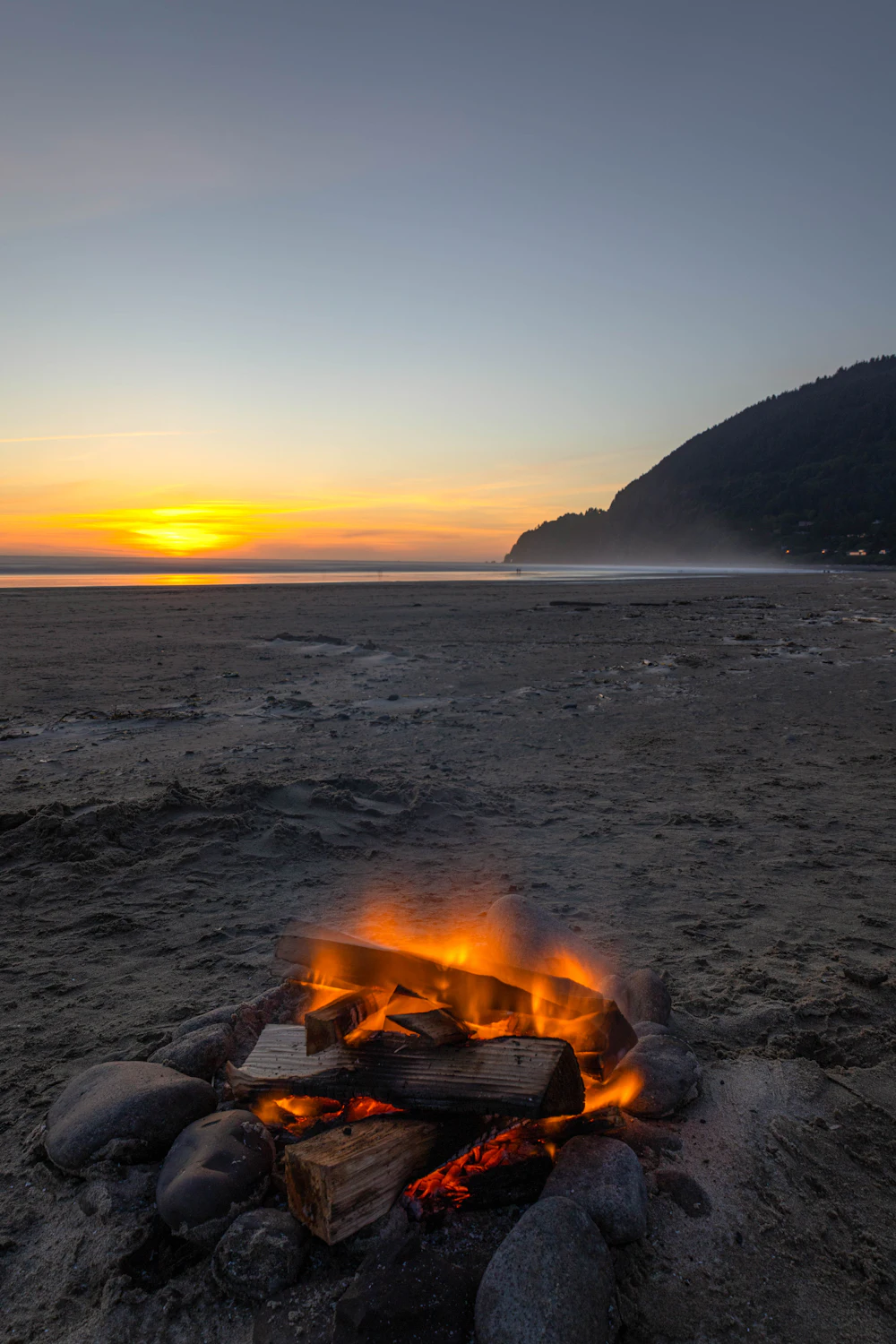 A campfire glowing on the beach as the sun sets over the ocean