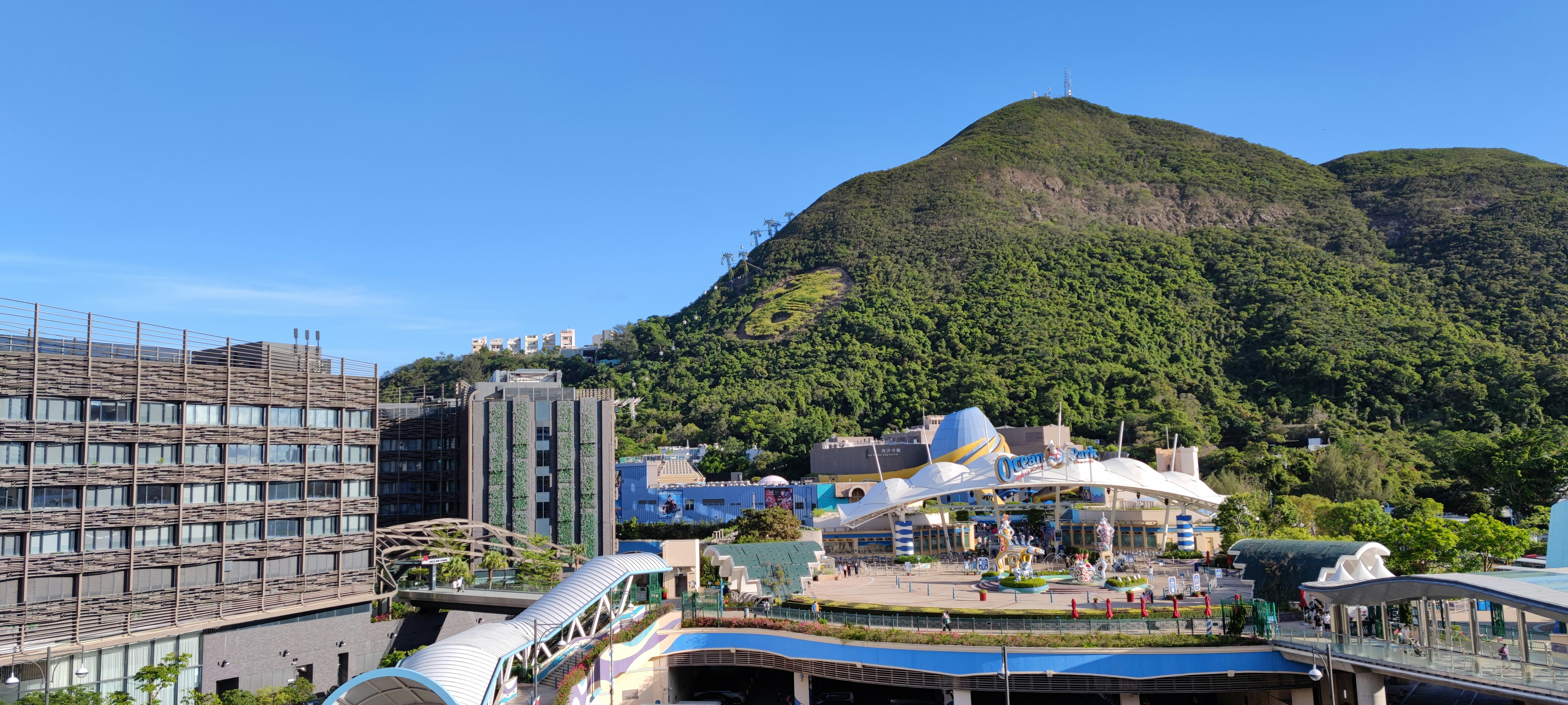 The entrance of Ocean Park, a tourist attraction and amusement park, in Wong Chuk Hang, southern district of Hong Kong Island. On the left is Hong Kong Ocean Park Marriott Hotel. The iconic sea horse symbol of Ocean Park is seen on the hill slope. Cable cars are running.