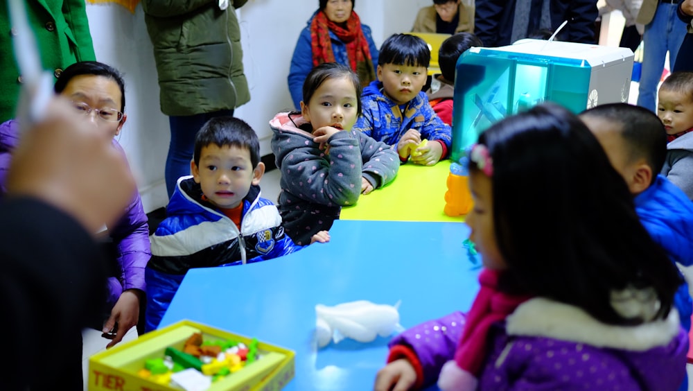 a group of children sitting around a blue table