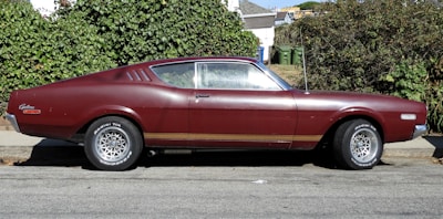 Compact burgundy coupe parked in front of a cozy Buda home.