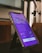 A smartphone is placed on a black stand showing a subscription page for an app. The screen displays a purple background with text about various features and pricing options, highlighting a 'Get Pro!' offer. The surrounding environment includes a blurred background and a metallic object nearby.