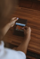 A person is holding an open wallet over a wooden surface, revealing a few cards including an ID and a credit card with contactless payment symbol. The person has light purple nail polish.