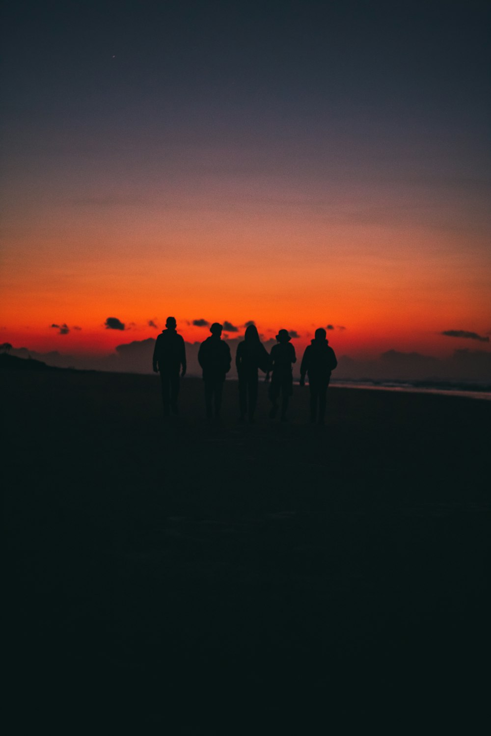 a group of people walking on a beach at sunset