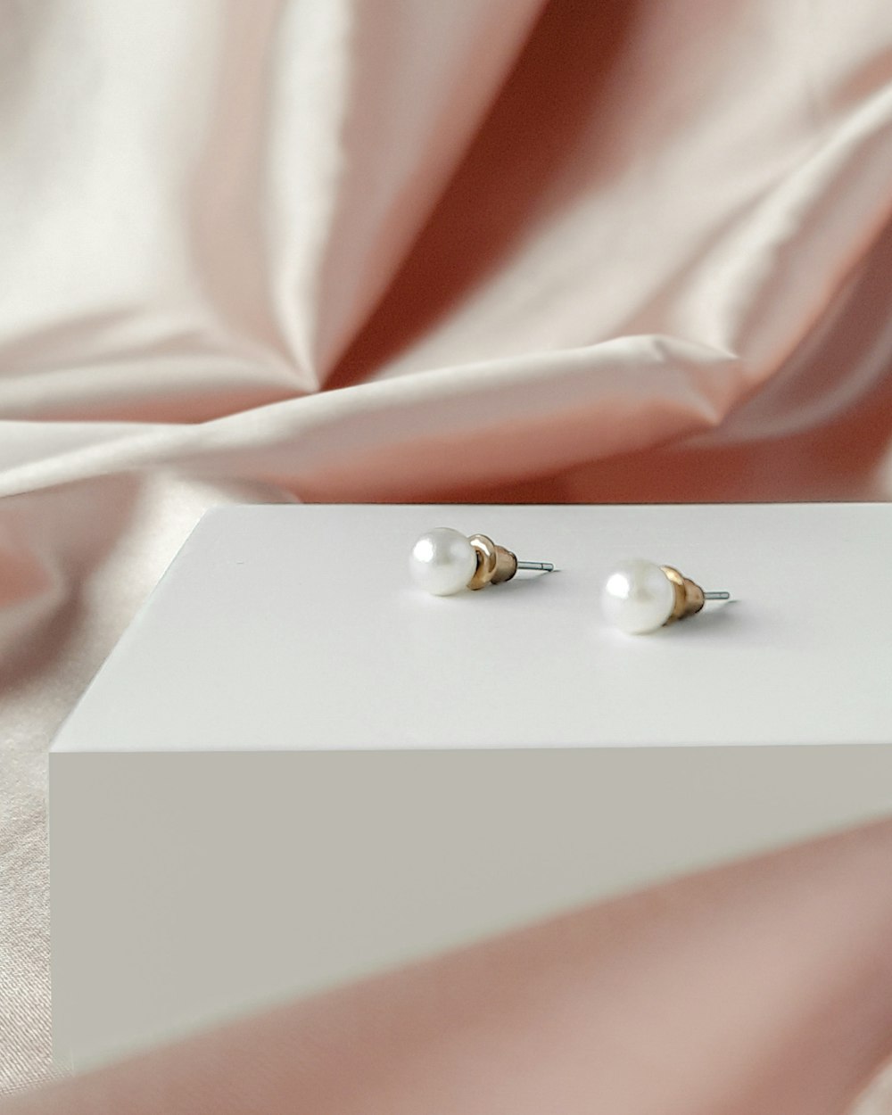 un paio di orecchini di perle seduti sopra una scatola bianca