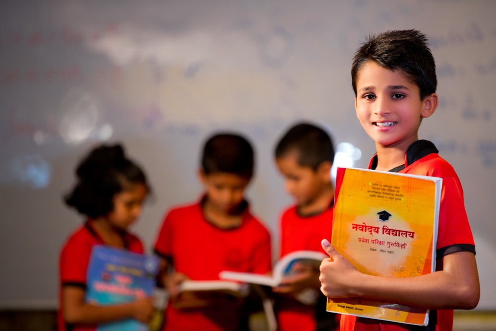 boy in red crew neck shirt holding yellow book