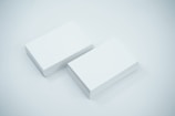 Two neat stacks of blank white business cards are placed side by side on a smooth, light-colored surface. The cards are uniformly aligned and appear crisp and clean.