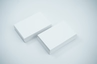 Two neat stacks of blank white business cards are placed side by side on a smooth, light-colored surface. The cards are uniformly aligned and appear crisp and clean.