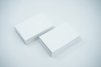 Two neat stacks of blank white business cards are placed side by side on a smooth, light-colored surface. The cards are uniformly aligned and appear crisp and clean.
