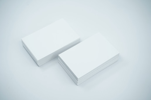 Two neat stacks of blank white business cards are placed side by side on a smooth, light-colored surface. The cards are uniformly aligned and appear crisp and clean.